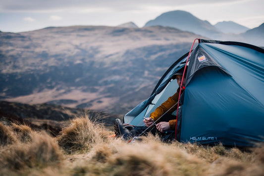 A small green tent pitched on a grassy ridge above a valley
