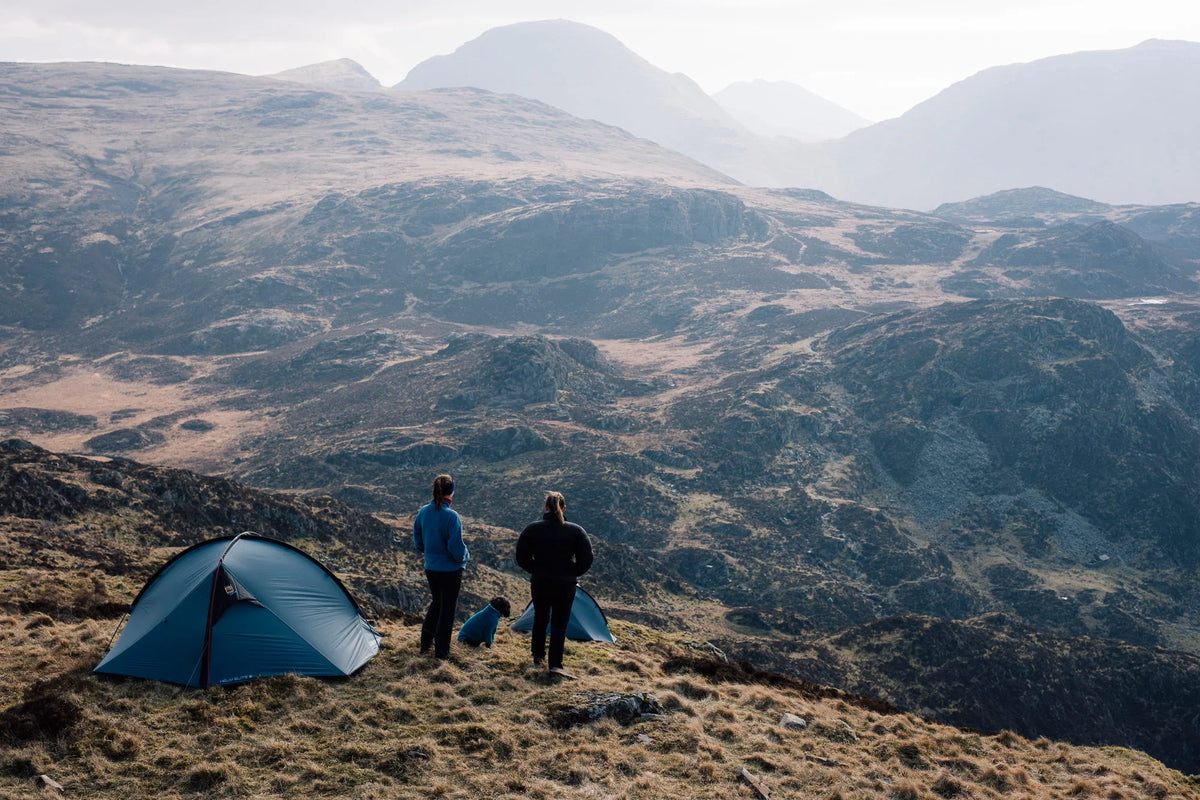 Two hikers stood next to the Helm Elite 2 tent on a mountain